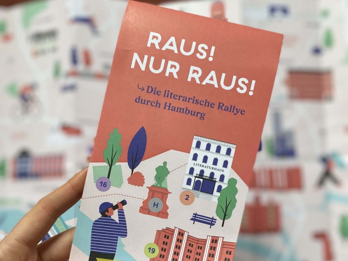 Der Flyer »Raus! Nur Raus! Die literarische Rallye durch Hamburg« wird über einen aufgefalteten Flyer gehalten.© Literaturhaus
