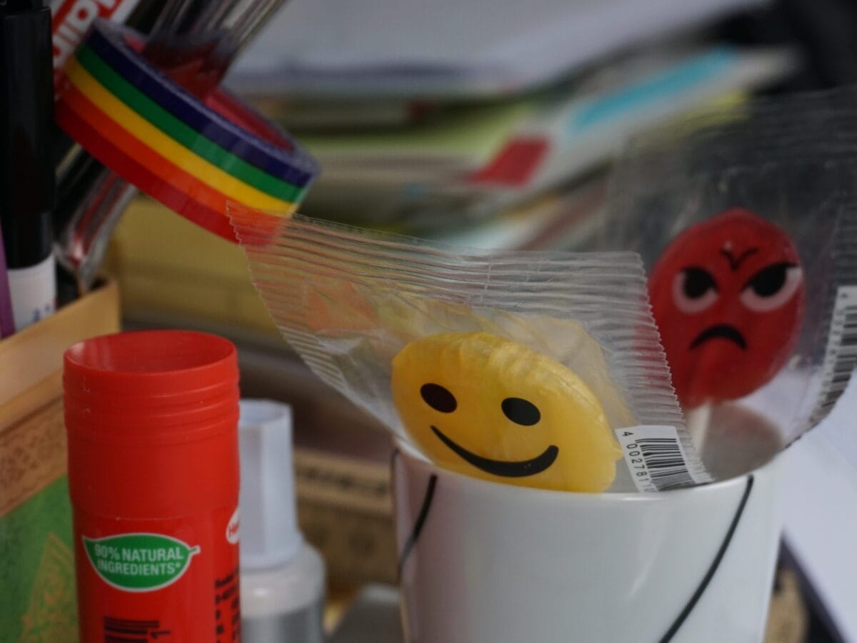 Blick auf eine Tasse, in der zwei Lollis stehen. Auf dem gelben Lolli ist ein fröhlicher Smiley zu sehen, auf dem roten ein böser Smiley.© Literaturhaus