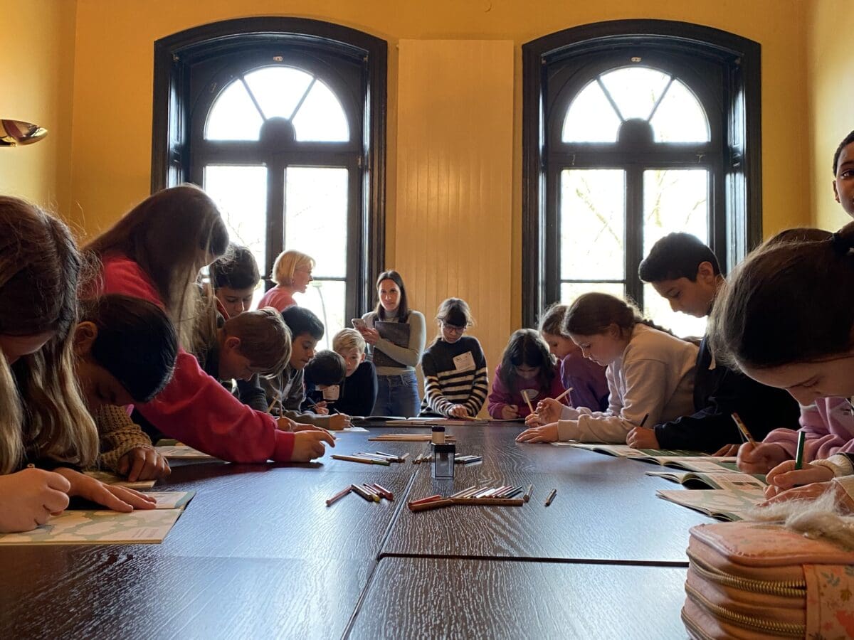 Eine lange Tischreihe. An beiden Seiten sitzen Kinder und malen und schreiben in den Gedankenfliger-Heften.© Literaturhaus