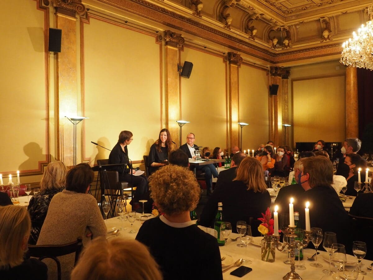 Feierlich hergerichteter Saal, auf den Tischen stehen Kerzenständer. Das Publikum blickt zur Bühne, auf der Stefanie vor Schulte mit zwei weiteren Personen sitzt.© Literaturhaus
