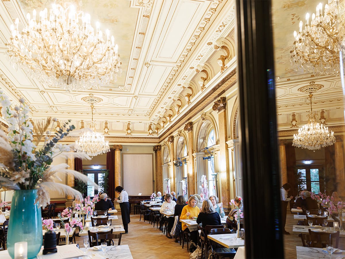 Der Eddy-Lübbert-Saal ist für den Cafébetrieb eingerichtet. An mehreren Tischen sitzen Menschen und trinken Kaffee.© Marcelo Hernandez