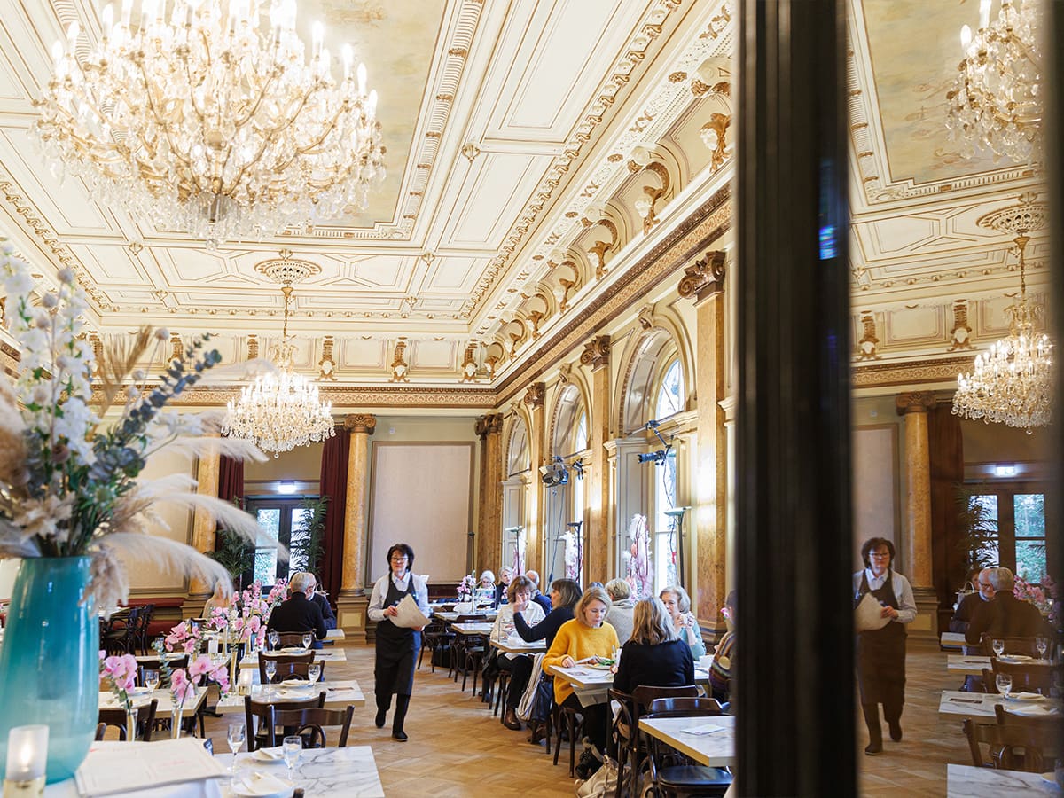 Der Eddy-Lübbert-Saal ist für den Cafébetrieb eingerichtet. An mehreren Tischen sitzen Menschen und trinken Kaffee.© Marcelo Hernandez