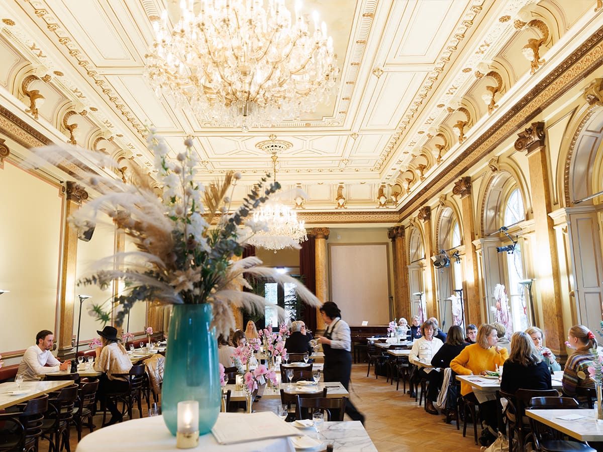 Der Eddy-Lübbert-Saal ist für den Cafébetrieb eingerichtet. An mehreren Tischen sitzen Menschen und trinken Kaffee.© Marcelo Hernandez