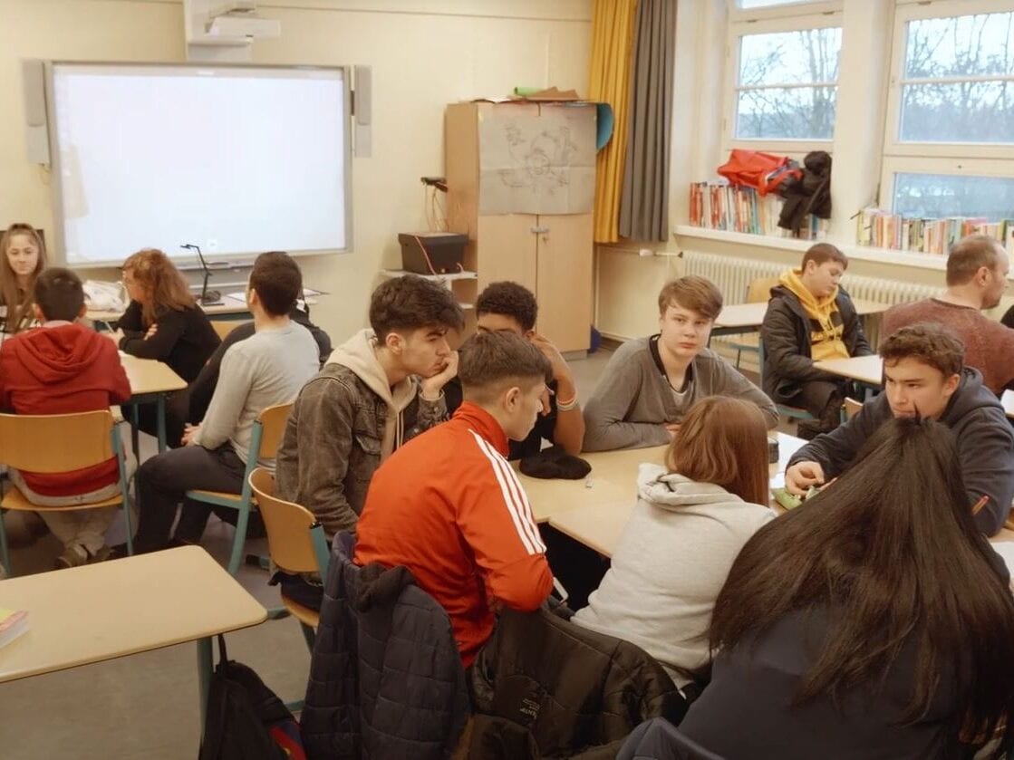 Screenshot des Videos: In einem Klassenraum sitzen Jugendliche an Gruppentischen und diskutieren.